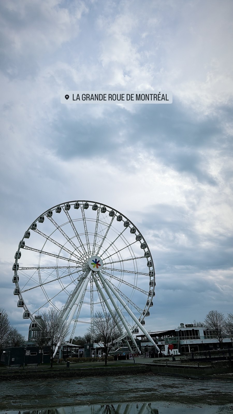 Wide social frame of La Grande Roue de Montreal under a cloudy sky